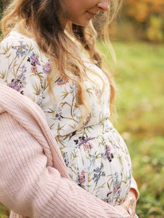 Woman holding hands with maple leaf on her pregnant belly, focus on hand