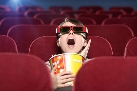 Shoked young woman with popcorn in 3D movieの写真素材