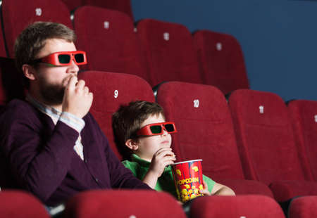 A boy with father eating popcorn in 3D movie theater