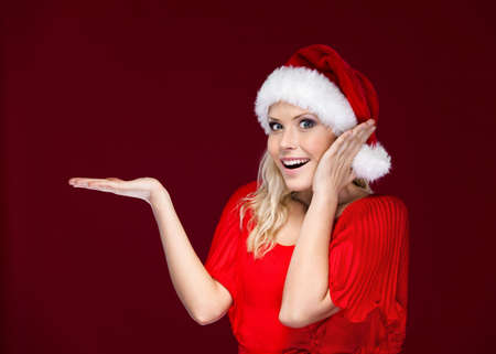 Woman in Christmas cap gestures palm up, isolated on purpleの写真素材