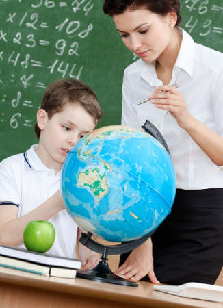 Geography teacher explains something to the pupil pointing at the globeの写真素材