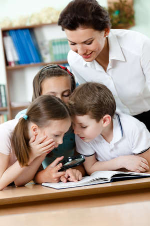 Young teacher with her pupils examine something with loupeの写真素材