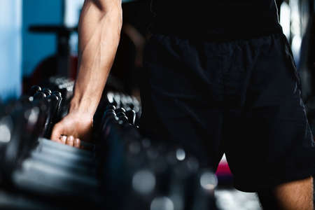Hand of a man choosing a dumbbell out of set of black dumbbells
