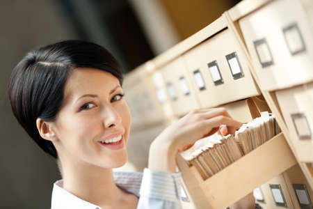 Woman seeks something in card catalog composed of set of wood boxes at the library. Study