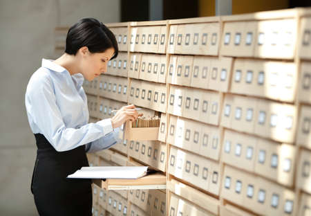 Woman seeks something in card catalog composed of set of wood boxes at the library. Knowledgeの写真素材