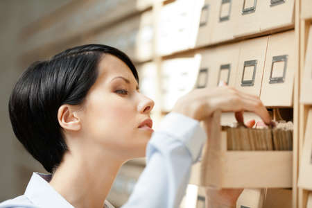 Woman searches something in card catalog composed of set of wood boxes at the library. Learningの写真素材