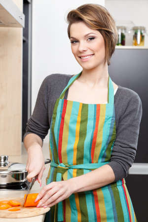 Young girl in striped apron chops vegetables in the modern comfortable kitchenの写真素材