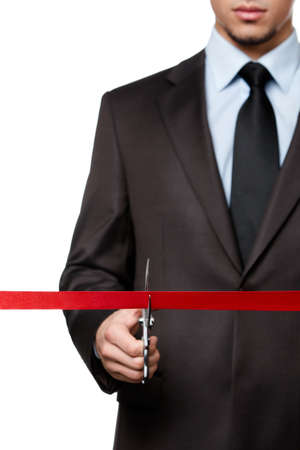 A business man cutting a red ribbon with scissors, isolated on whiteの写真素材