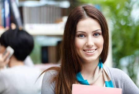 Woman student at the library against bookshelves and her friend. Study