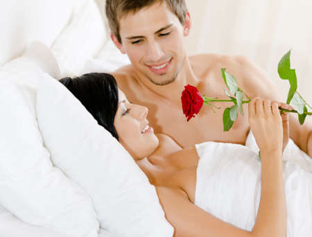 Man lying in bed-room gives scarlet rose to woman  Concept of love and affectionの写真素材