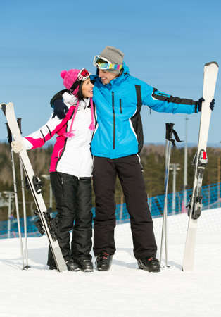 Full-length portrait of two embracing skiers with skis in handsの写真素材