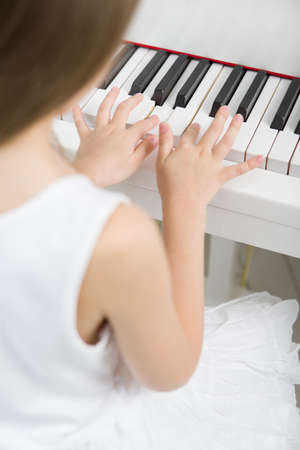 Back view of little girl in white dress playing piano. Concept of music study and artsの写真素材