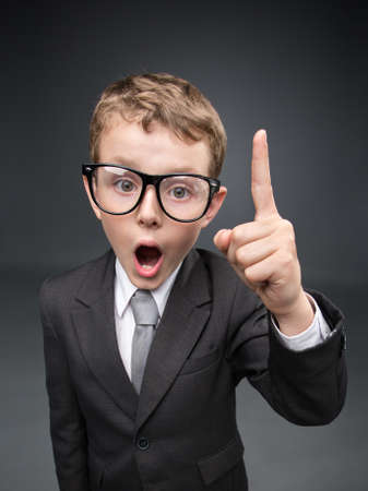 Wide angle portrait of little businessmen in spectacles forefinger gesturing, on grey background. Concept of leadership and successの写真素材