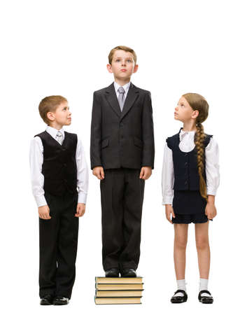 Full-length portrait of little boy standing at pile of books among other children, isolated on...