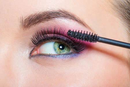Close up of female eye with bright makeup and brush applying mascara on eyelashesの写真素材