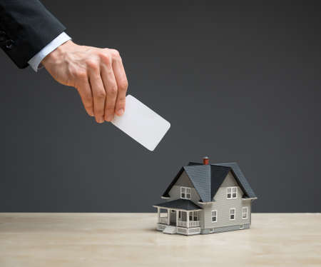 Close up of little house and hand with copyspace on grey background. Concept of real estate and investmentの写真素材