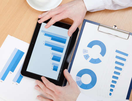 Top view of business man working on the tablet with diagrams. Close up of hands and graphs