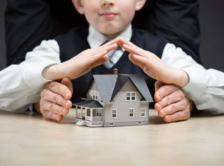 Little boy puts hands as roof over house model. Concept of real estate and protectionの写真素材