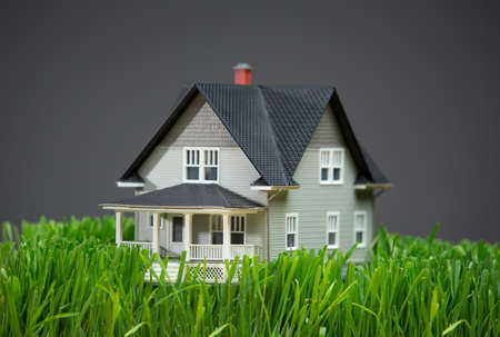Close up of home model with green grass on grey background. Concept of realty and buildingの写真素材