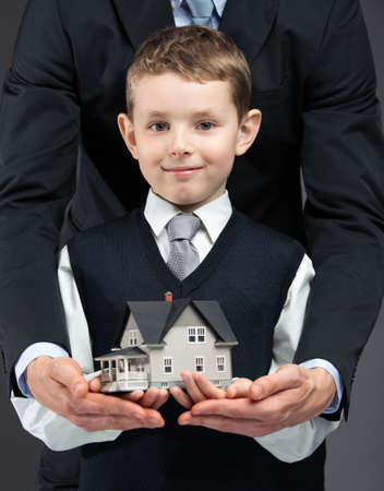Close up of little boy and somebody's hands keeping house model. Concept of real estate and businessの写真素材