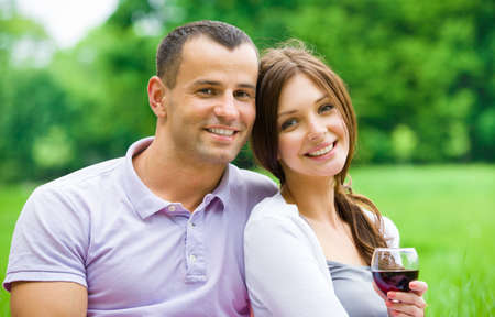 Attractive couple drinks wine in park. Concept of romantic dating and loveの写真素材