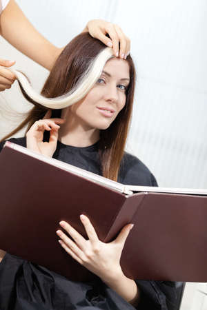 Hairdresser tries lock of dyed blond hair on the client sitting on the chair in the hairdresser'sの写真素材