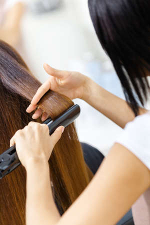 Backview of hair stylist doing hair style for woman in hairdressing salon. Concept of fashion and beautyの写真素材