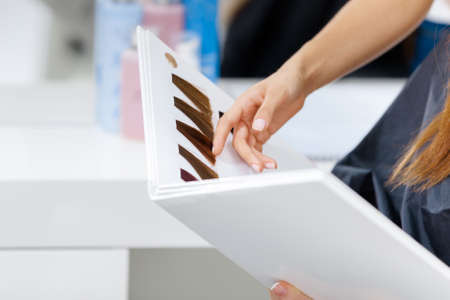 Close up of book with dyed hair color samples and hand showing it. Concept of beauty and careの写真素材