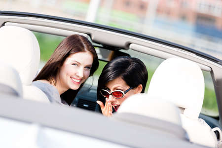 Two happy girls sitting in the car turn back and have fun while having little car trip