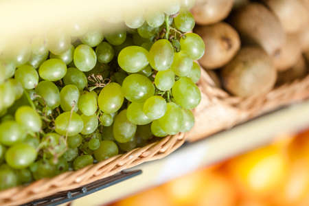 Close up of grape and fresh kiwis in the braided basket. Concept of healthy foodの写真素材