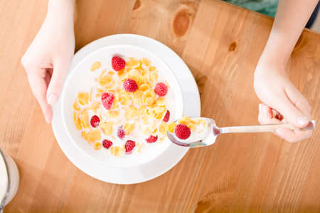 Top view of hands of the girl eating muesli with strawberry and milkの写真素材