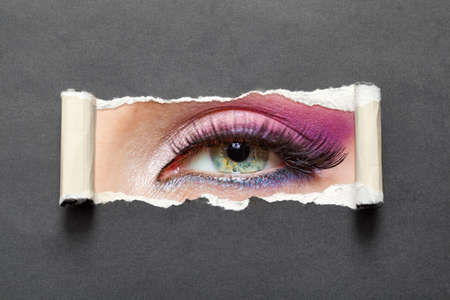 Close up of female eye with pink make-up on torn paper. Concept of fashion and beauty.の写真素材