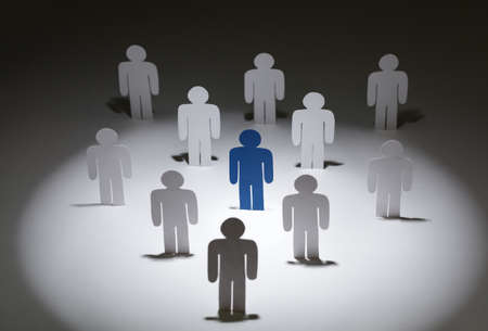 Close up of team of standing paper-men. Lots of similar copies of a paper man, but a blue one stands out among them. Concept of teamwork and leadershipの写真素材