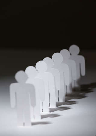 Close up of group of papermen standing in a row. Lots of copies of one paper man on black backgroundの写真素材