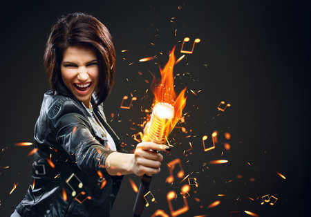 Half-length portrait of female rock musician handing mike on fire, grey backgroundの写真素材