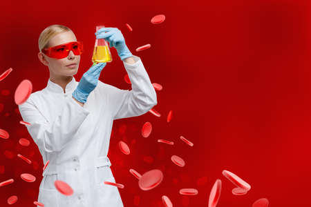 Woman doctor hands Erlenmeyer flask with yellow water on red blood cells backgroundの写真素材