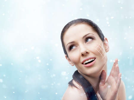 Woman applying face cream in to have smooth perfect skin, snowy background. Body care conceptの写真素材