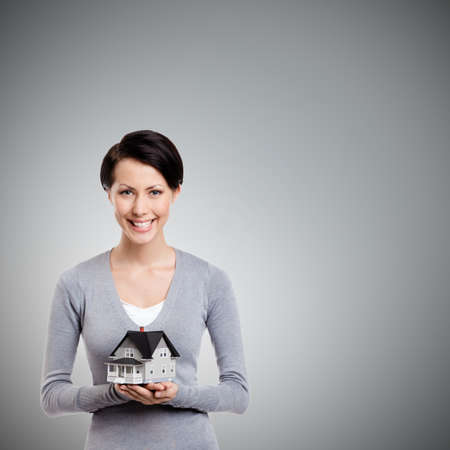 Young woman hands small toy house in front of herself, isolated on greyの写真素材