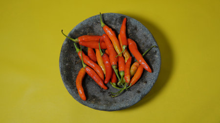 Red hot chili peppers in a stone plate on a yellow background. some red chilies on a pestle with a...