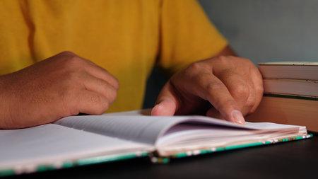 someone in yellow is reading something in a notebook. Man reading a book in the library. Close up of hands.の写真素材