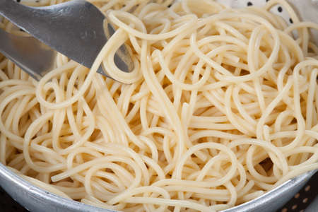 Spaghetti in a colander with pasta tongsの写真素材