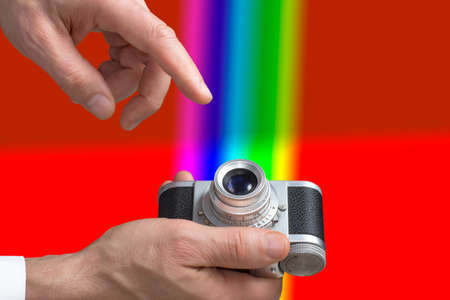 Close view of a vintage camera in mans hands in a  red rainbows background.