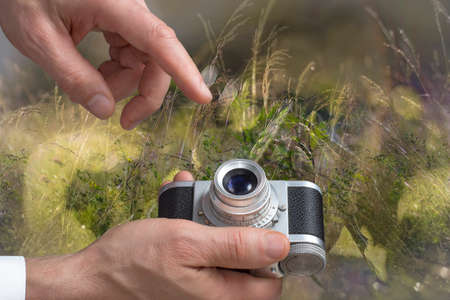 Close view of a vintage camera in mans hands in a blurred meadows background.の写真素材