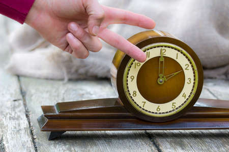 Mechanical and electronic time. A clock on the table and two fingers near it.の写真素材