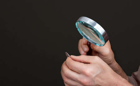 Mans hands with a loupe and an ancient silver coinの写真素材