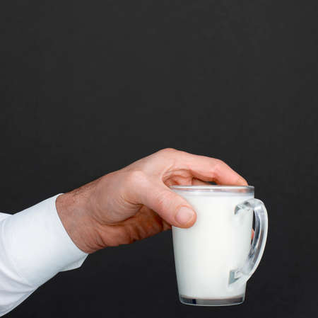 Mens hand with a cup of milk in a dark background