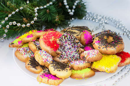 White plate with colored biscuits in a white background with jewelry and green pineの写真素材