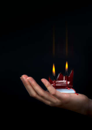 Female hands holding a red double flamed flat candle in a dark backgroundの写真素材