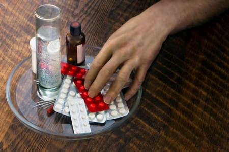 Patients hand takes medicines from the plate on the table