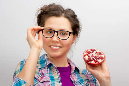 Smiling young woman with eyeglasses and pomegranate  in a white backgroundの写真素材